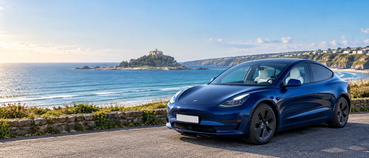 A ZensCars private hire car parked on a Cornish coast road, with the sea and St Michael's Mount behind